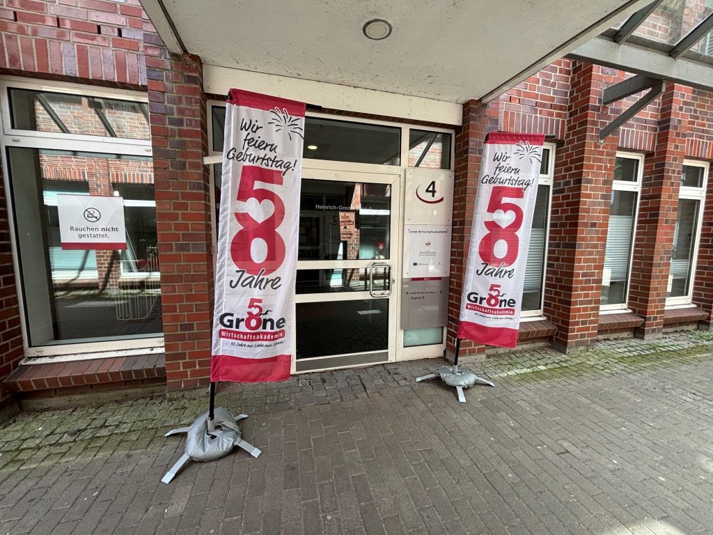 Das Foto zeigt zwei Jubiläum-Beachflags vor dem Eingang der Grone Wirtschaftsakademie
