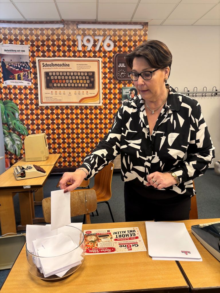 Eine Akademieleiterin wirft ihren Beitrag für die Tombola in das Glasgefäß in der Grone Wirtschaftsakademie.